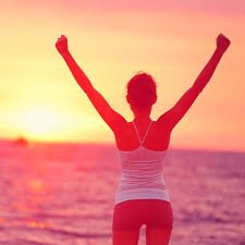 Woman on a beach at sunset with her arms raised